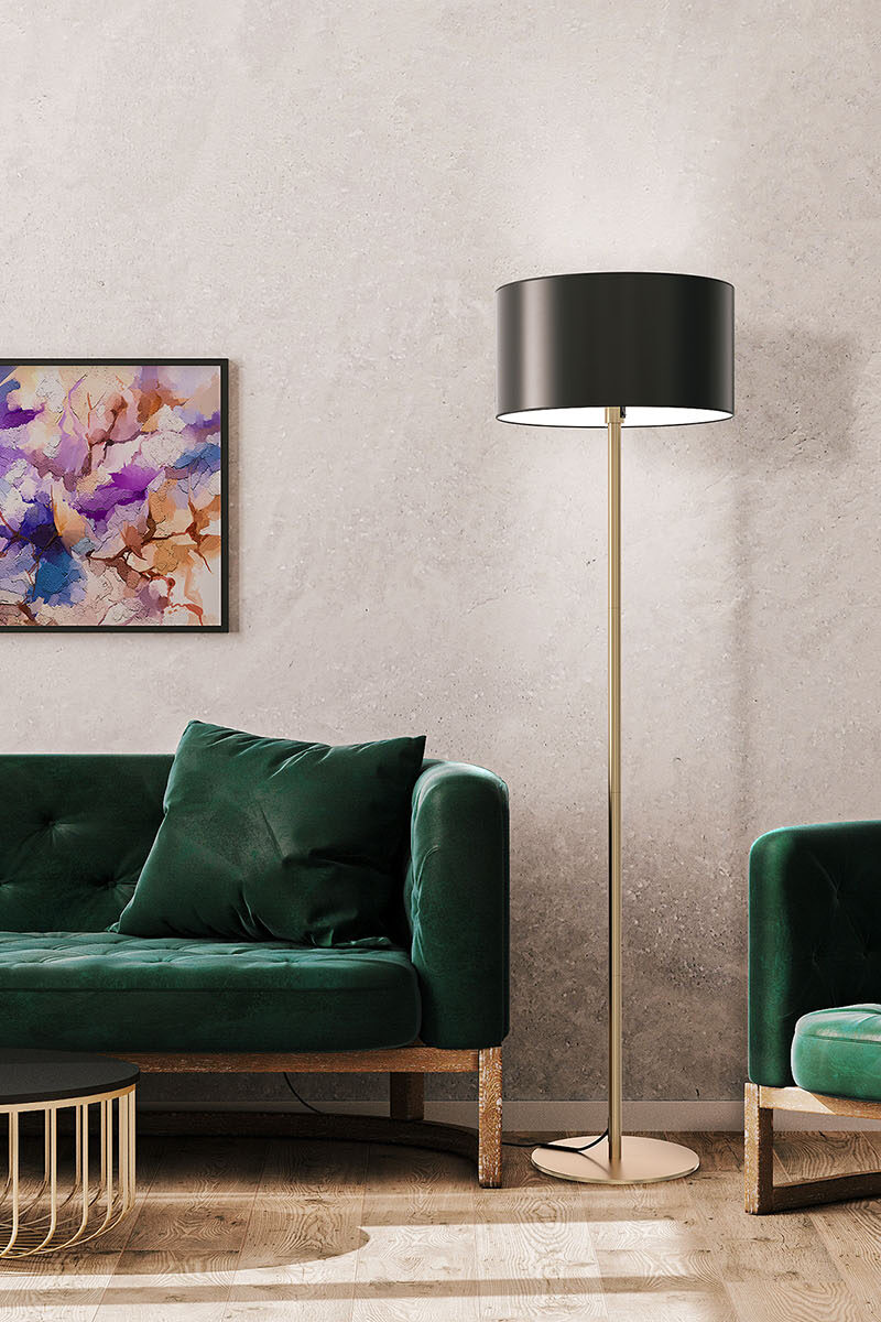 Tyylikäs lattiavalaisin mustalla varjostimella ja messinkisellä rungolla vihreän sohvan rinnalla valoisassa huoneessa.